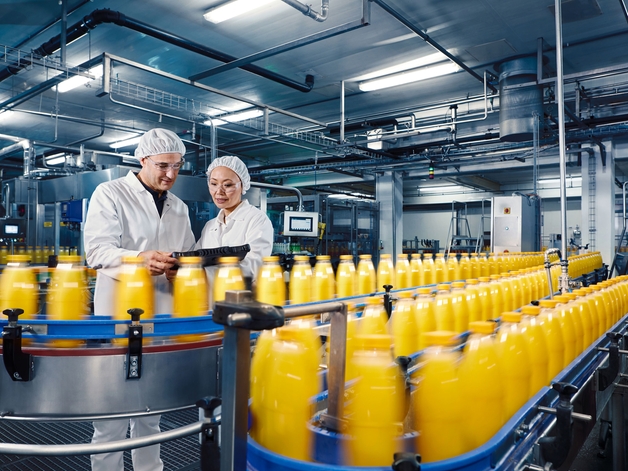 To teknikere i et tappeanlæg overvåger påfyldningsprocessen for appelsinjuice.